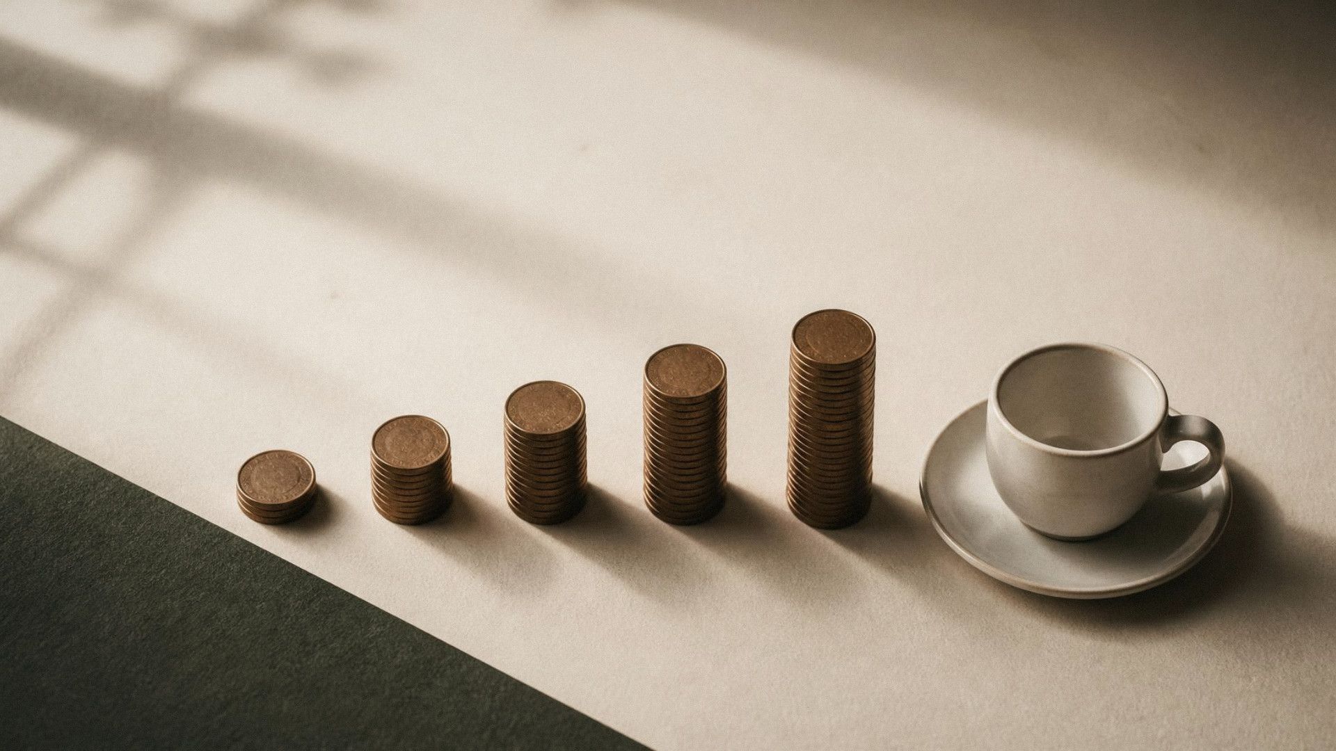 Five stacks of coins growing taller from left to right, ending at an empty espresso cup