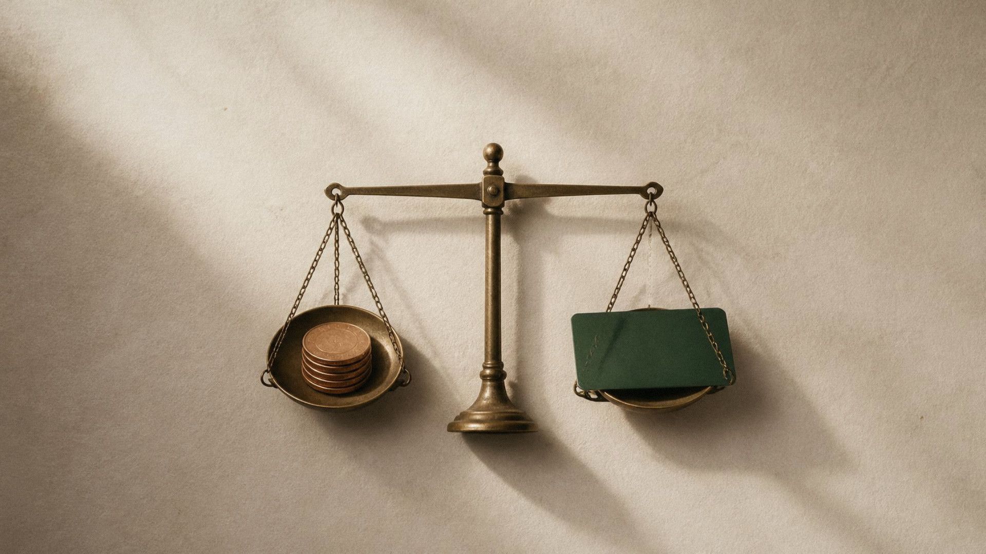A brass balance scale with a stack of coins on one side and a green card on the other