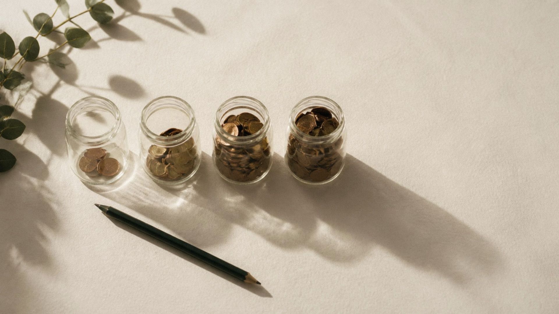 Four glass jars holding more coins from left to right, with a pencil beside them